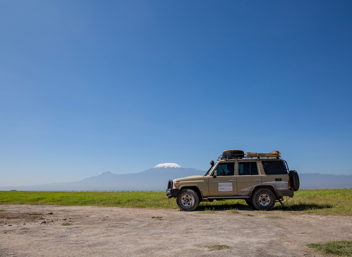Wide open plains with acacia trees and Mount Kilimanjaro towering in the distance over Amboseli National Park