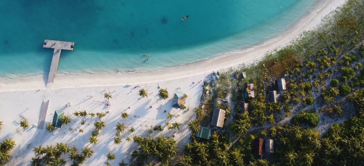 Aerial view of a whitewashed beachfront resort with palm gardens and infinity pool overlooking a turquoise bay on the Watamu coast of Kenya