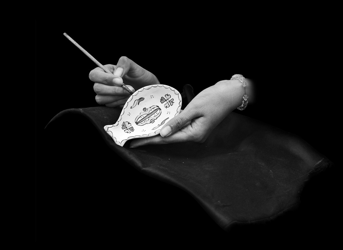 close-up of a Kazuri artisan's hands hand-painting a ceramic pendant with a fine brush