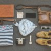 An open duffel bag packed with neutral-colored safari clothing, binoculars, and a camera on a lodge bed in Kenya