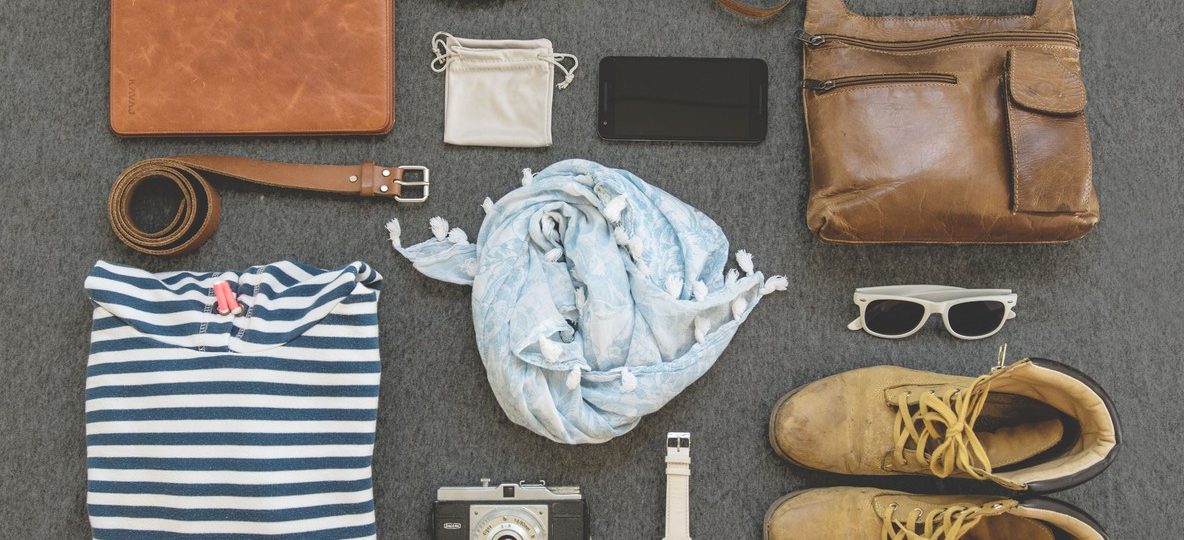 An open duffel bag packed with neutral-colored safari clothing, binoculars, and a camera on a lodge bed in Kenya