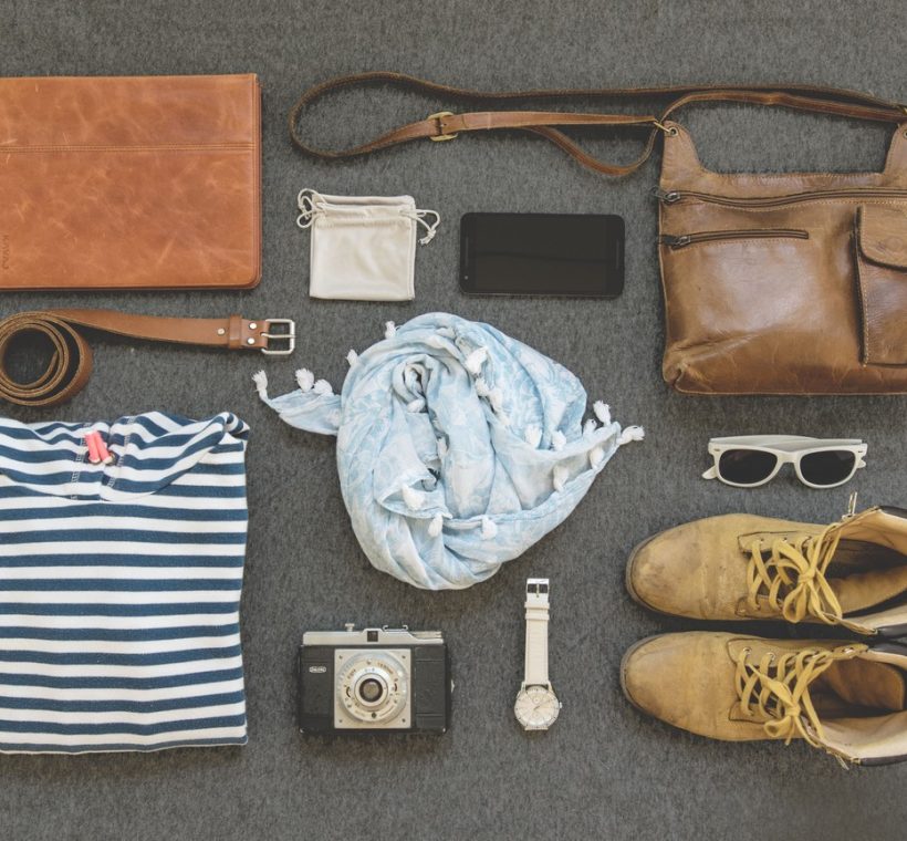 An open duffel bag packed with neutral-colored safari clothing, binoculars, and a camera on a lodge bed in Kenya