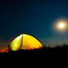 An open-air safari tent glowing at night under a star-filled sky and rising moon in the Kenya bush